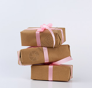 包装在着棕色Kraft纸和白色背景上与粉丝带捆绑在一起的盒子中叠礼物图片