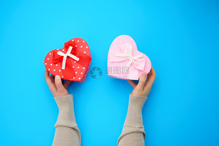 两只女手握着红和粉色纸板盒以蓝背景的心脏形状顶部视图图片
