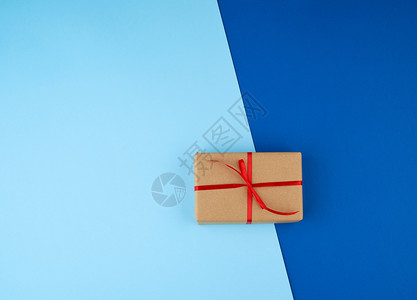 包着棕色的Kraft纸与蓝色背景的红薄丝带绑在一起假日情人节周年生日图片