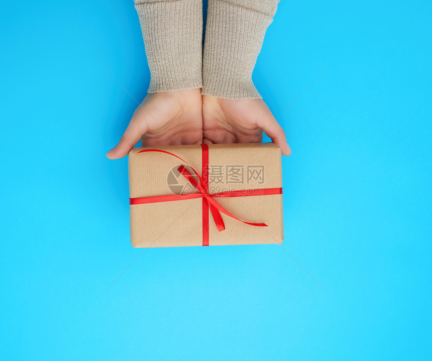 女手握着一个棕色的盒子蓝背景上有红弓祝贺生日快乐的概念文本位置图片