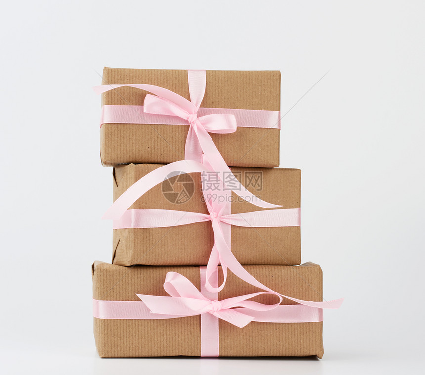 包装在着棕色Kraft纸和白色背景上带丝绑在白色背景上的盒子中一叠礼品图片