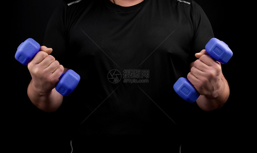 穿黑色制服的成年男子运动员手握蓝色塑料哑铃黑背景图片