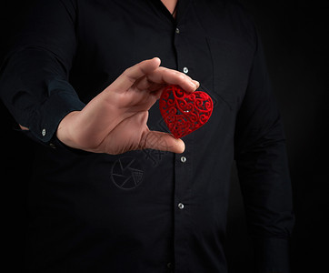 成人男子身穿黑衬衫背着暗景身衬衫在右手胸前握着红心将爱的概念放在胸前图片