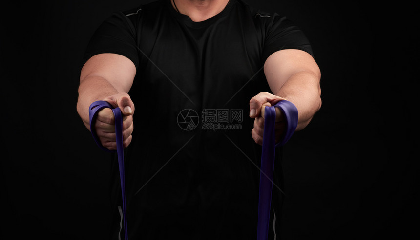 身穿黑衣肌肉的运动员正在用低密钥紫色橡胶进行体操图片