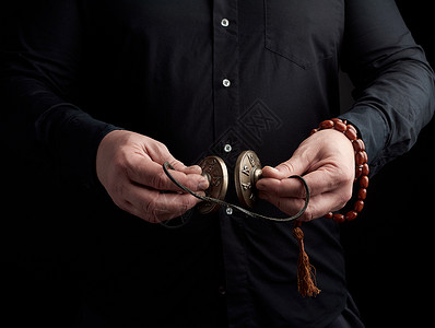 印度仿制药身着黑衣服的成人男子手里握着一对用皮绳宗教仪式用物冥想和替代药低键的铜制Karatal背景