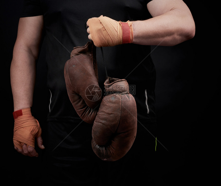 身穿黑色制服的肌肉运动员手上握着非常古老的棕色拳击手套被用橙色弹运动绷带黑色底绷带绑上图片