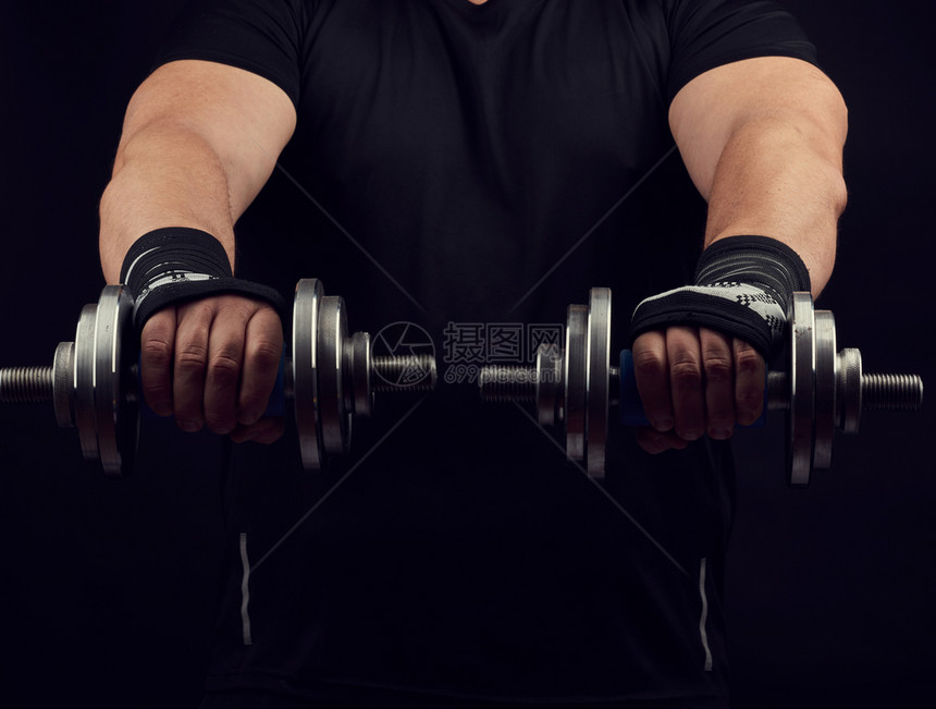 穿黑衣服的成年男子手上握着钢铁哑铃肌肉紧张低钥匙运动背景图片