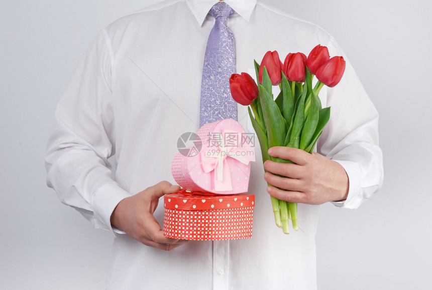 白衬衫和领带的成年男子拿着一束红郁金香花绿色的叶子和礼物盒白色背景的礼物盒生日快乐的概念周年纪日情人节约会图片