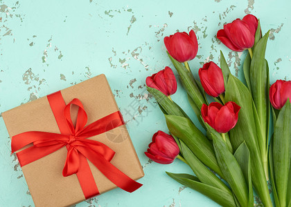 红色盛开的郁金香花束配有绿色叶子棕手工艺纸包着的礼物以及绿色背景顶层观点的丝绸红色带生日情人节的喜庆背景背景图片
