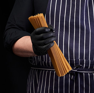 戴黑色乳胶手套的厨师条纹围裙持有用黄面小麦制成的面原生长条图片