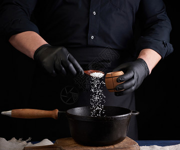 黑制服和乳胶手套的男烹饪用黑色铸铁锅制成盐类食品晶体在空气中冻低键图片