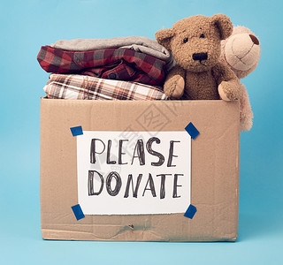 玩具盒子大棕色纸板盒上面有刻字请捐赠盒子里装满各种衣服蓝底玩具背景