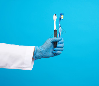 医生治疗师穿着白袍制服和蓝色无菌手套持牙刷日常概念蓝背景图片