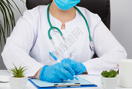 白大衣女医生无菌的学手套在表格上写处方治疗师坐在白桌子的椅上工作场所图片