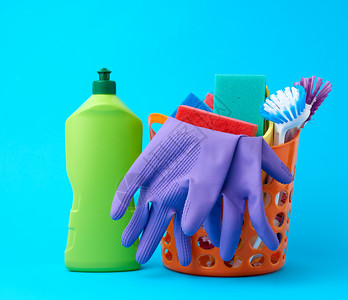 蓝底绿色塑料瓶装有冲洗海绵橡胶保护手套刷子和清洁剂的橙色篮子图片