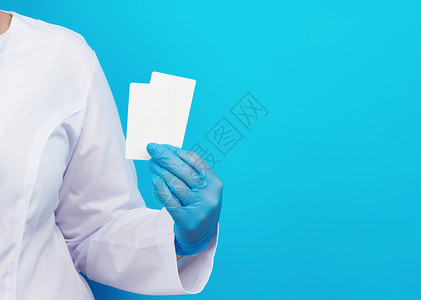 名片蓝色医生用蓝色胶手套在蓝色背景登记地点的空白纸面名片上持有一张空白纸面名片背景