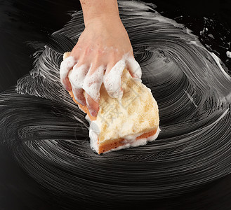 黑色海绵白色肥皂泡沫中的女手握着湿海绵擦黑表面清洁和洗涤表面的概念最高视线背景