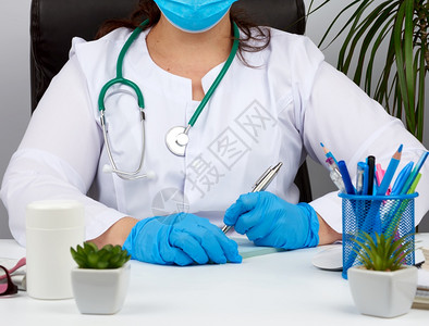 白大衣女医生无菌的学手套在表格上写处方治疗师坐在白桌子的椅上工作场所背景图片