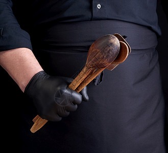 穿黑色乳胶手套的厨师和穿黑色制服的将木质旧勺子放在他面前低键图片