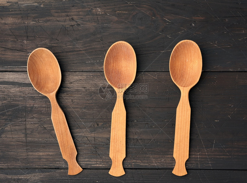 3个空木勺子在棕色背景上从顶部的板图片