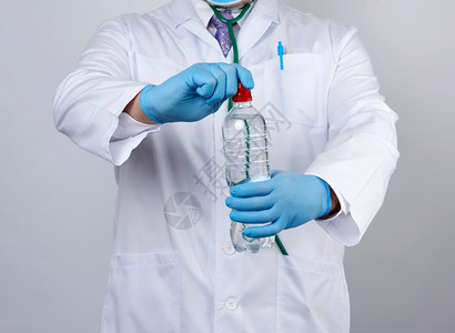穿白色大衣和蓝乳胶手套的医生持有透明水瓶人类消费概念图片