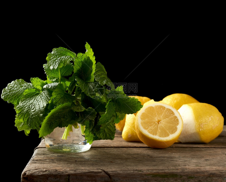 黄色成熟的柠檬和木板上一串新鲜绿色薄荷柠檬汁的原料黑色背景图片