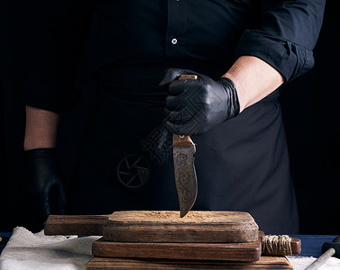 穿黑衬衫和乳胶手套的厨师拿着一把老式厨房刀用于切肉低键图片