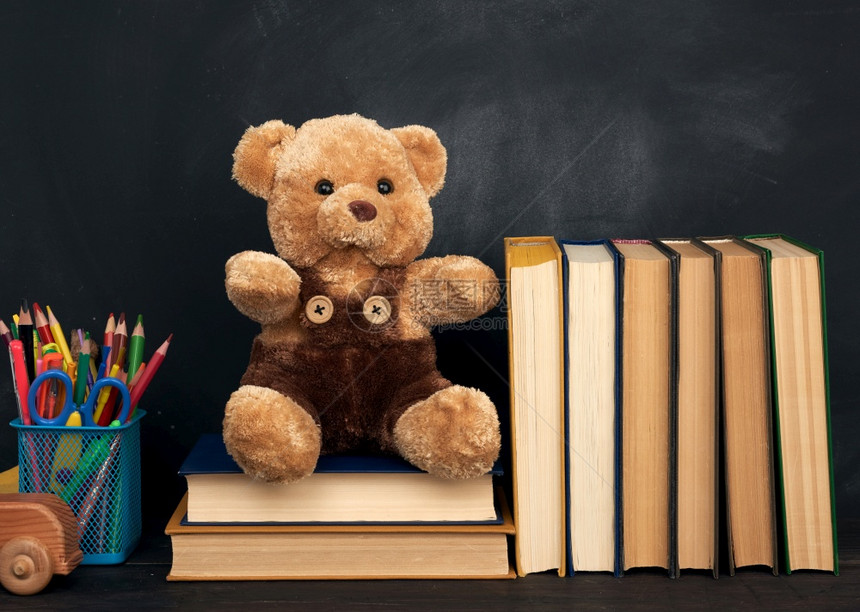 棕褐色泰迪熊坐在棕木桌上坐在空黑粉笔板后面回到学校图片