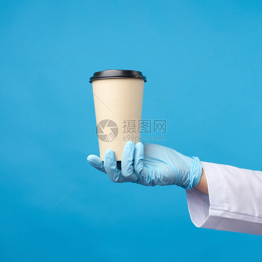 在流行病期间用蓝色胶手套握着一张纸次面板杯和蓝色背景的塑料遮罩安全无接触地在线发送订单图片