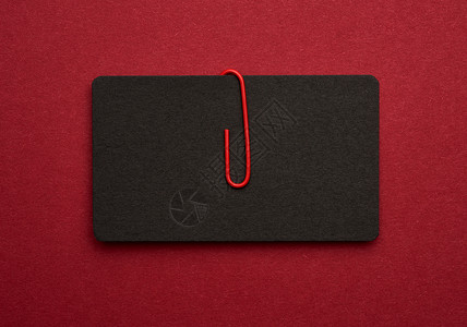 黑色纸板名片和红色金属回形针在红色背景上俯视图平放图片
