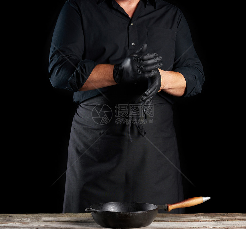 厨师穿黑色衬衫和围裙在准备食物黑人背景之前将黑色乳胶手套戴在上图片