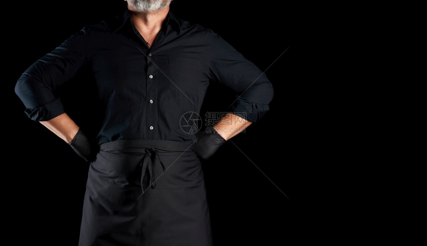 黑衣厨师和乳胶手套站在黑色背景上手放在臀部图片