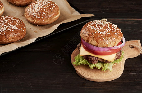 芝士汉堡加西红柿烧烤切片和芝麻面包放在旧木切板上棕色背景图片