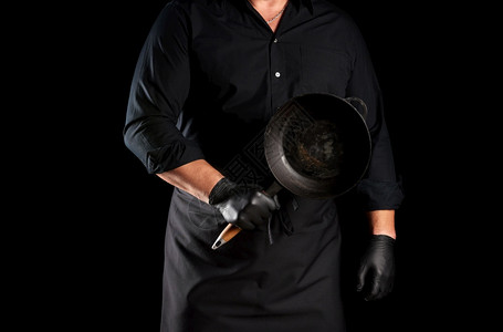 穿黑色制服和乳胶手套的男厨师在前面拿着一个空的圆旧黑色铁铸板低键图片