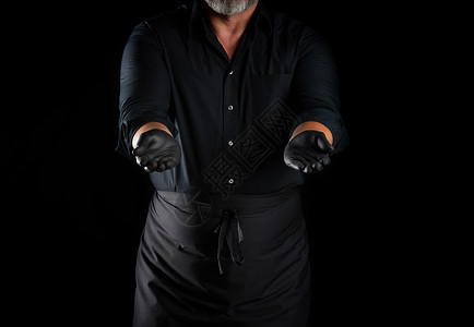 黑衬衫厨师围裙和乳胶黑手套站在色背景上他的手臂伸展持有物件背景图片