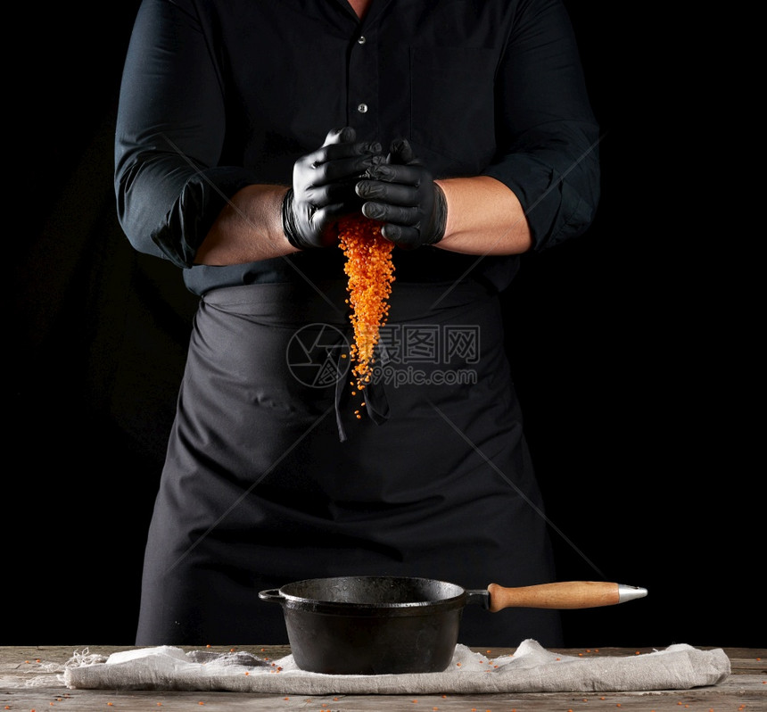 黑衣服主厨和乳胶手套将生扁豆倒入圆制铁锅手柄黑色背景图片