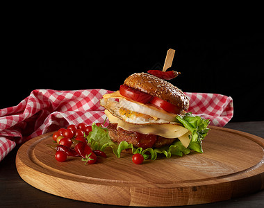 美味的汉堡肉饼奶酪煎蛋番茄黄瓜切片绿生菜圆木板上快餐黑底图片