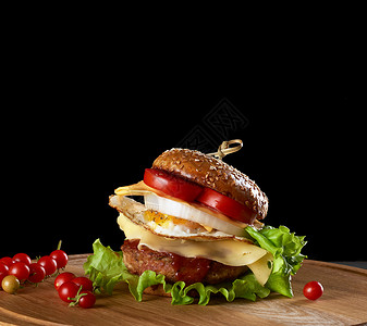 美味的汉堡肉饼奶酪煎蛋番茄黄瓜切片绿生菜圆木板上的快餐黑色背景图片