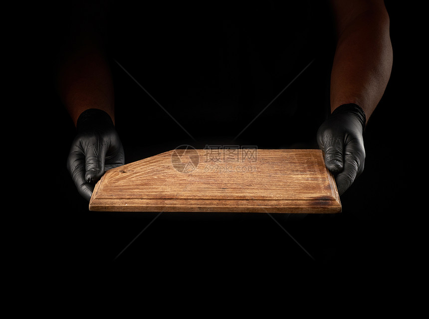 黑乳胶手套的雄握着黑色背景的空旧棕木切削板图片