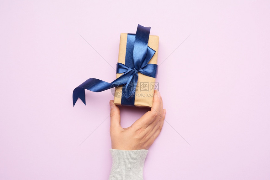 女手拿着一个礼物纸盒放在紫色背景喜庆顶视图上图片