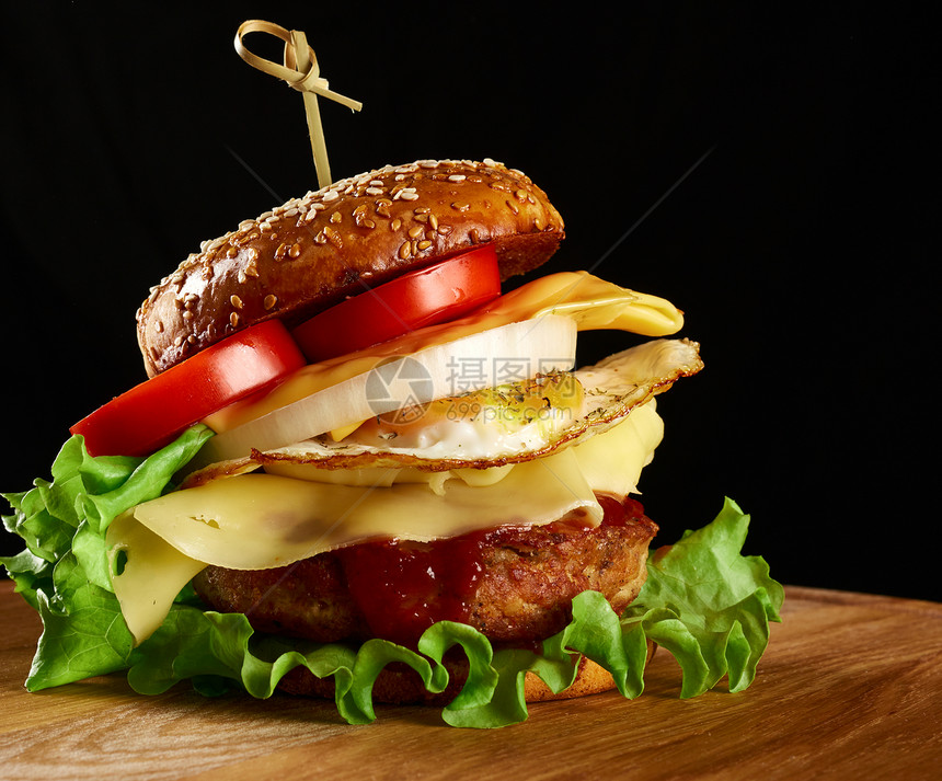 汉堡加肉饼奶酪煎蛋西红柿黄瓜切片绿生菜圆木板上的快餐黑色背景图片