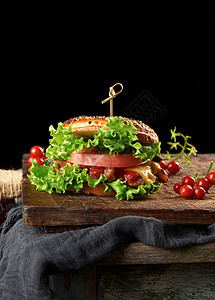 在木制棕色厨房板上加肉绿色生菜和番茄酱的芝士汉堡背景图片