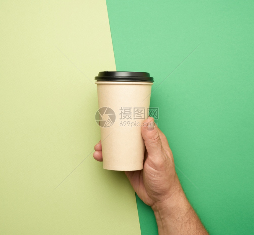 在绿色背景环保零废物的概念上握着棕纸一次杯的男手图片