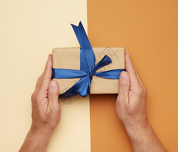 男手拿着礼物盒在棕色背景上鞠躬为假日赠送礼物的概念图片
