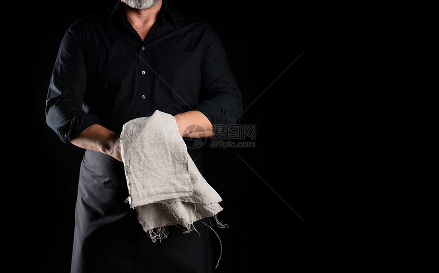 穿黑色围裙和衬衫的男厨师在黑色背景作记号的地方持有灰色纸巾图片
