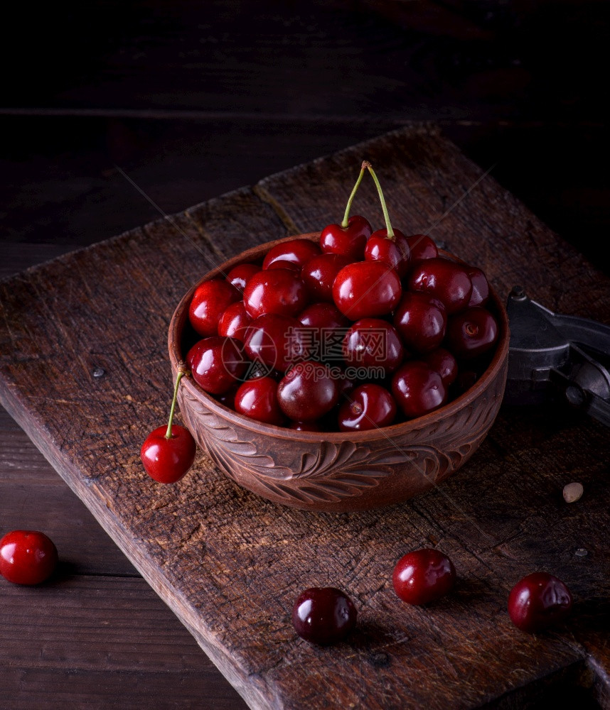 熟的红多汁甜樱桃在棕土碗中木制桌子上关闭图片