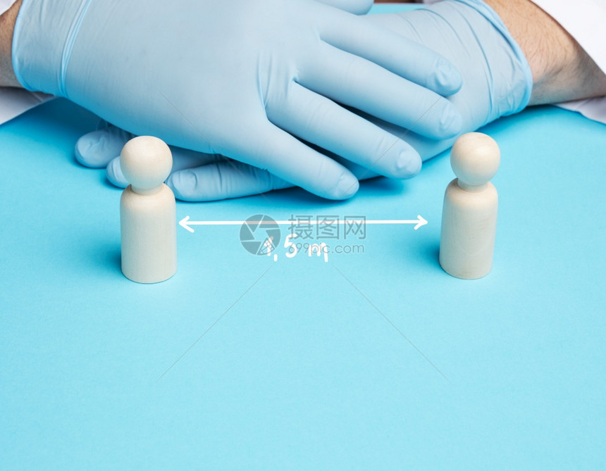 两名木制男子站在身着蓝色乳胶手套的医生男背景上在流行病和期间保持1米半的距离图片
