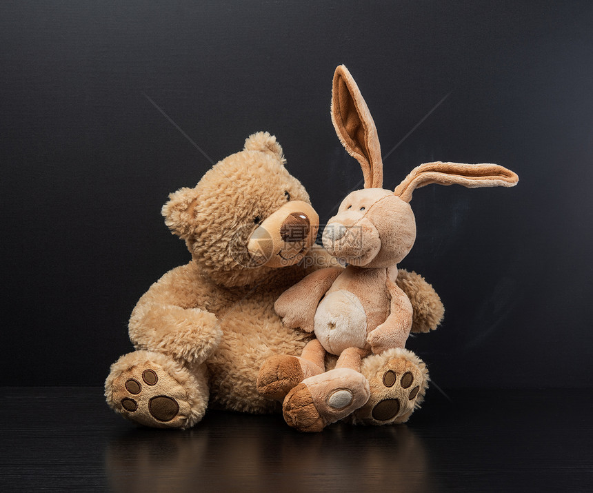 棕褐色泰迪熊在黑粉笔板背景上抱着一只泰迪兔子跪在膝上图片