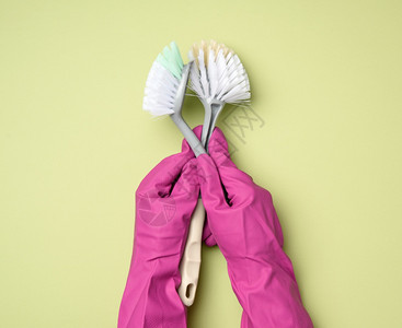 穿紫色橡皮手套的女握着绿色背景的塑料清洁刷子关上图片