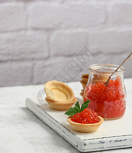 玻璃罐中的红鱼子酱和白桌上的圆帆布关上图片